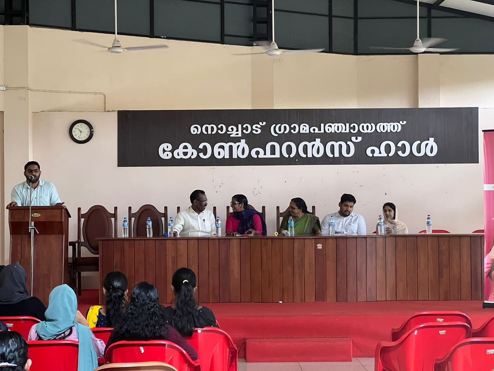 Jeevana MD Muhammed Shahim speaking from the podium alongside T.P. Ramakrishnan MLA at Nochad Grama Panchayath Hall